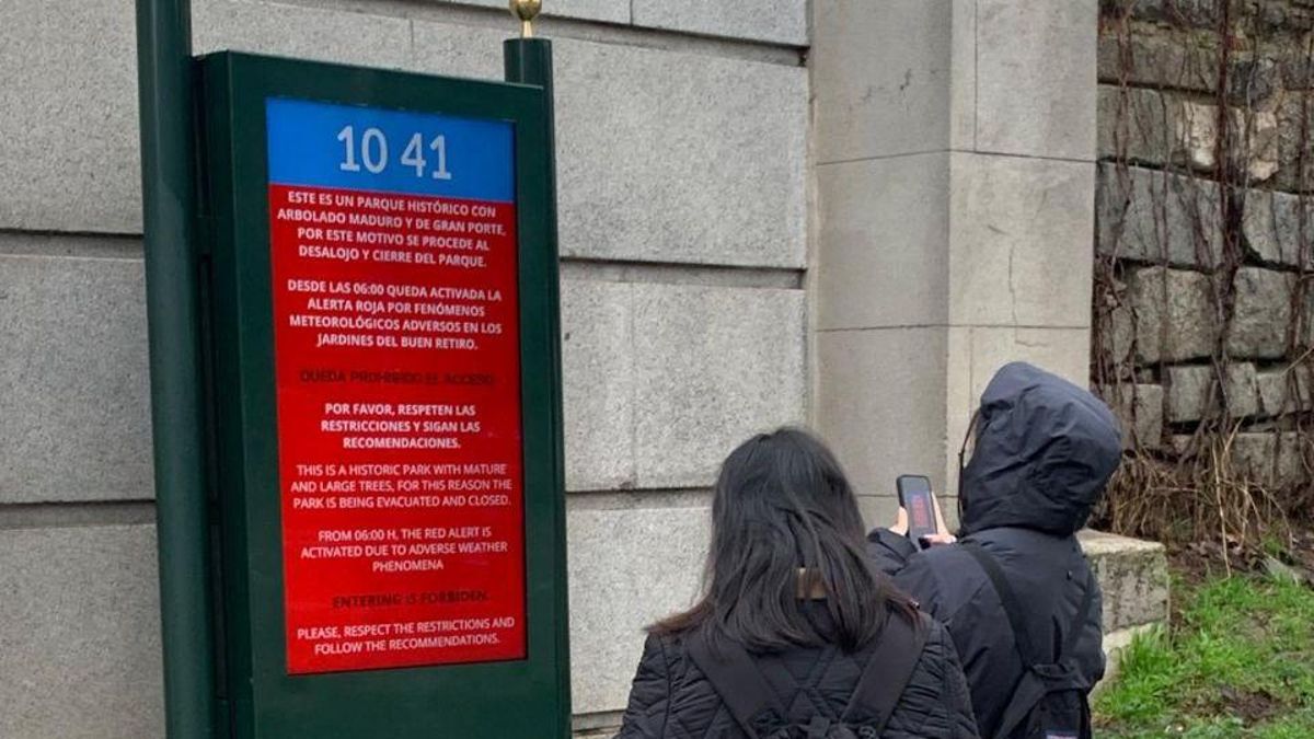Turistas observan un cartel con el cierre del Retiro en un día de alerta roja y traducen el mensaje en su móvil.