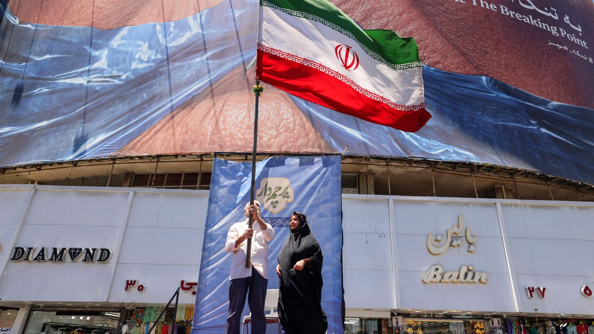 Un hombre hace ondear una bandera de Irán en plaza Valiasr de Teherán el 26 de mayo ante la mirada de una mujer.