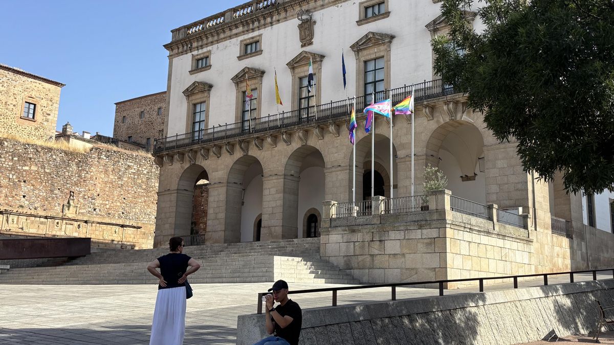 Varias personas junto al Ayuntamiento de Cáceres donde ondean las banderas del Orgullo LGTBI, este domingo