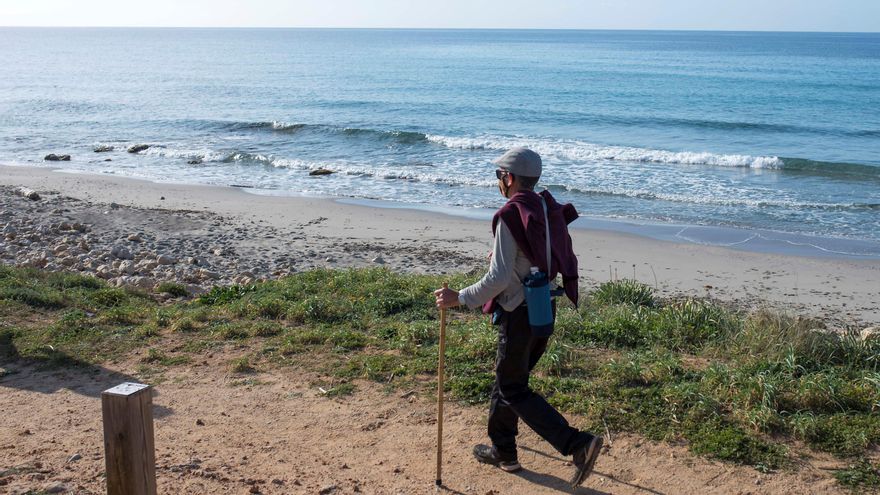 Un hombre pasea por Camí de Cavalls en Menorca a su paso por la playa de Binigaus.