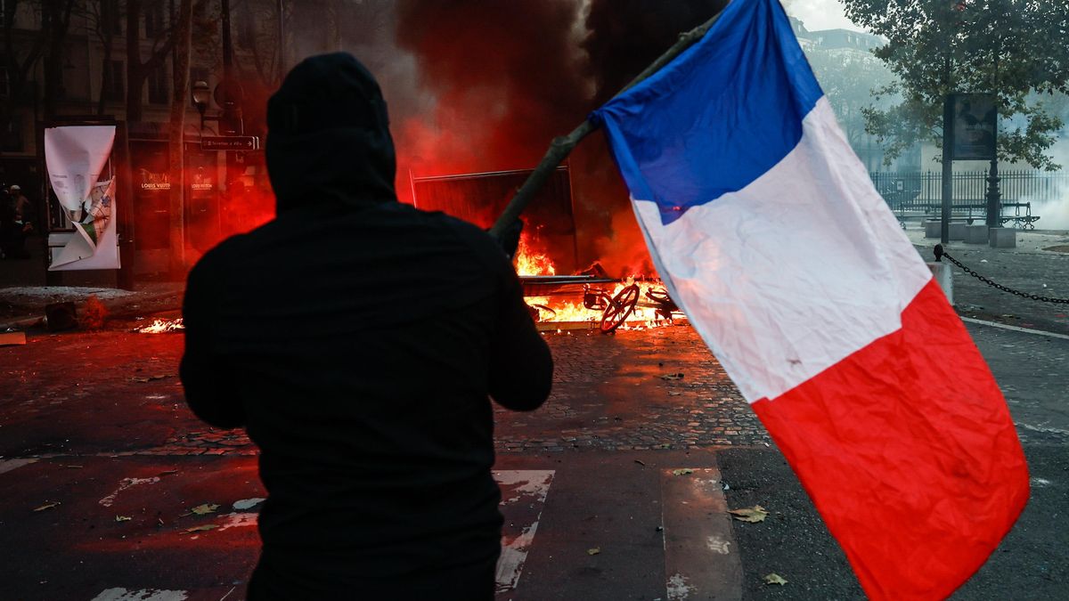 Un manifestante con una bandera francesa se enfrenta a la policía en la Plaza de la Madeleine, en París, el 17 de octubre de 2026.