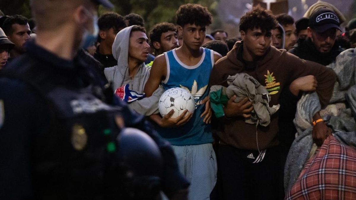 Los migrantes empiezan a ser dirigidos hacia el nuevo campamento levantado por el Gobierno con 864 plazas. Van a pie. Los de la primera fila, se agarran mientras caminan custodiados por la Policía