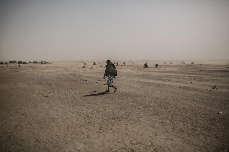 Una mujer atraviesa el desierto en dirección al campo de refugiados de Kindjandi.  En este campo de refugiados más de 40 mil personas desplazadas y refugiadas encontraron un lugar seguro. Al llegar las familias del pueblo ofrecieron agua, comida y materiales para construir refugios. Agua i comida son las necesidades básicas que las pesonas que buscaron aqui refugio no puede satisfacer, a veces suelen pasar dos o tres días sin comer. La falta de agua limpia y comida han llevado a la comunidad a una situación dramática donde muchas familias no llegan a un plato de comida diario.