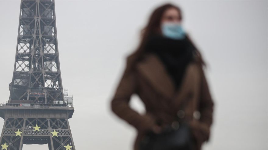 Una mujer con mascarilla pasea junto a la Torre Eiffel de Paris.