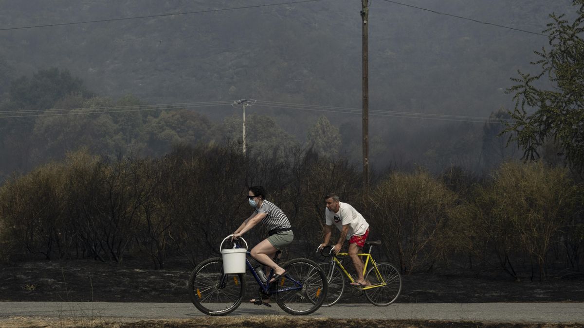 Dos personas, una de ellas protegida con una mascarilla, circulan en bicicleta por una zona quemada debido al incendio de Monterrei (Ourense).