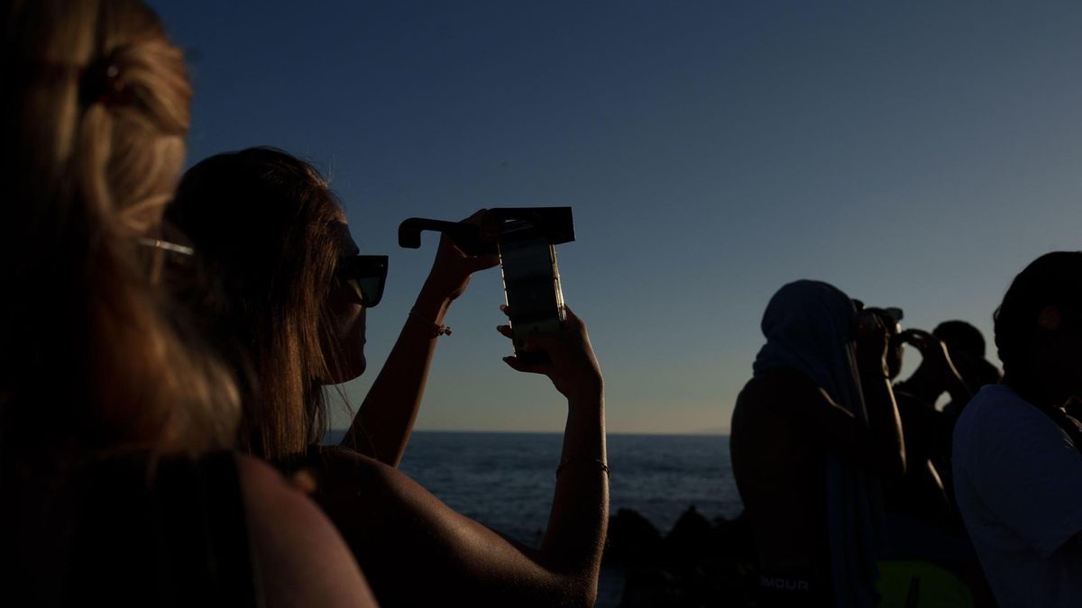 Varias personas contemplan desde la playa el eclipse solar, que se ha visto de forma parcial, este miércoles en el municipio tinerfeño de Guía de Isora.