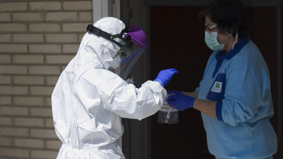 Un sanitario entrega las pruebas a otro, tras realizar una recogida de muestra desde el coche para detectar casos de coronavirus, (Covid-19), en el Hospital Militar de Sevilla.