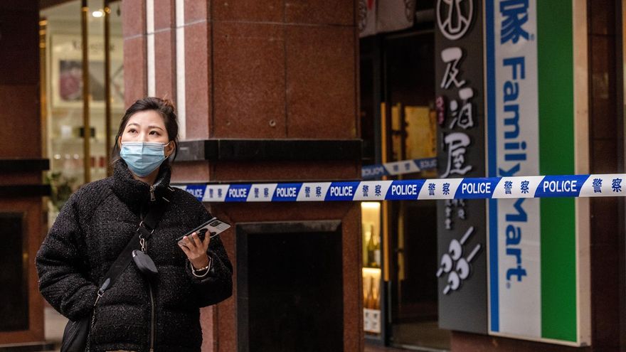 Una mujer pasa por una tienda cerrada por casos de Covid-19 y vigilada por una policía en Shanghai, China.