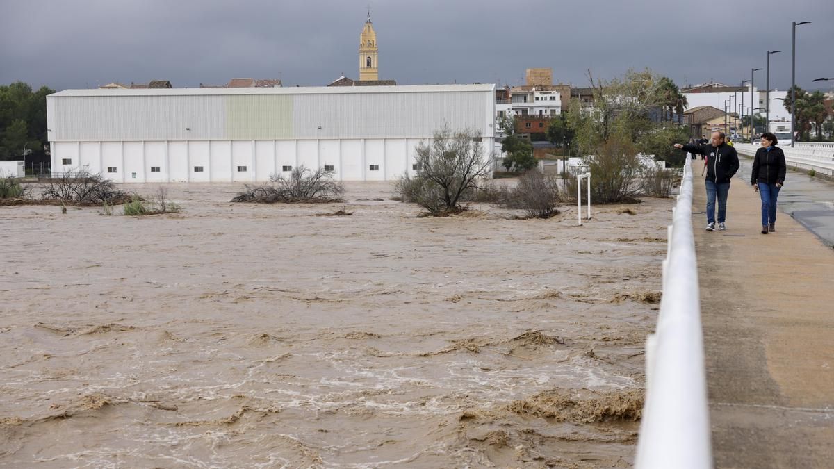 Dos personas contemplan el gran caudal del río Magre a su paso por Alfarp (Valencia) debido a las lluvias torrenciales que afectan a la Comunitat Valenciana, y especialmente a la provincia de Valencia, en la que se ha establecido el aviso rojo.