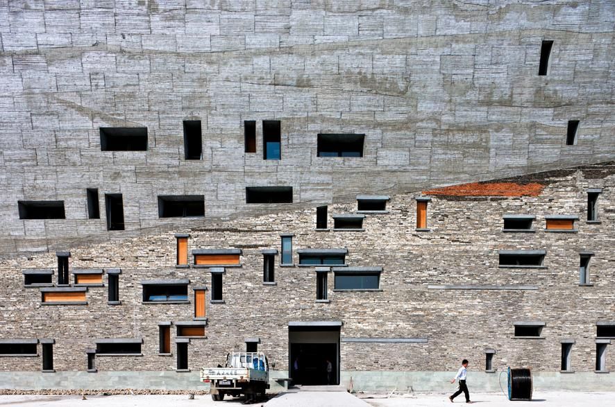 Amateur Studio-Wang Shu & Lu Wenyu, Museo de Historia, Ningbo Ningbo, Zhejiang, China, foto Iwan Baan Diseñado evocando las montañas, la planta muestra tres ‘desfiladeros’ —dos interiores, uno exterior— atravesados por escaleras. En el encofrado de los muros de hormigón se han utilizado troncos de bambú, una técnica poco habitual. El patio principal del museo atraviesa todo el volumen, llegando hasta la cubierta transitable. Su acabado a base de piezas de u-glass establece un potente contraste con el resto de las superficies.