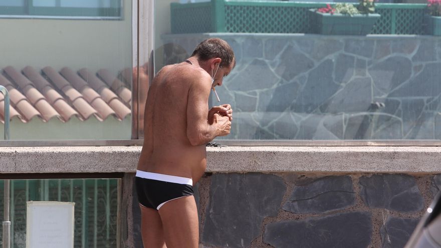 Un hombre se baja la mascarilla para fumar aleado de otras personas en la playa de Las Brurras.