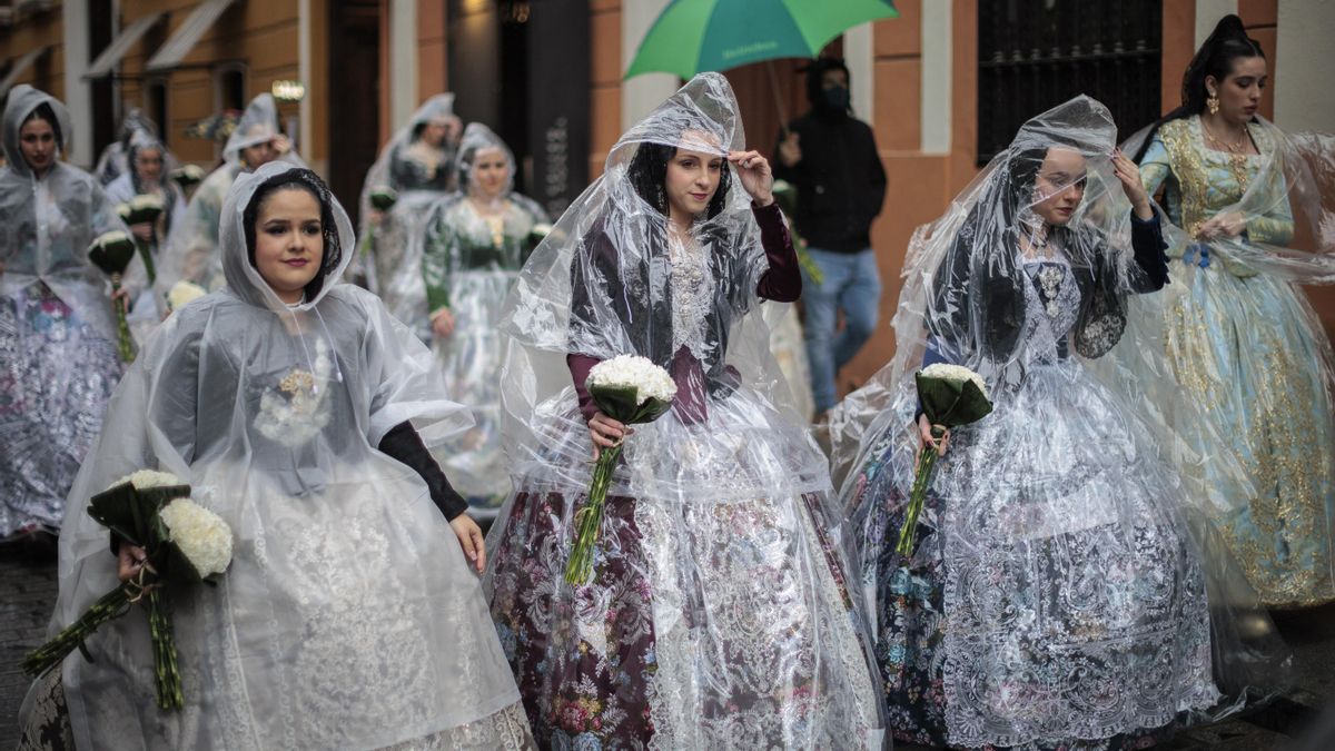 Falleras protegen sus vestidos de la lluvia durante la ofrenda.