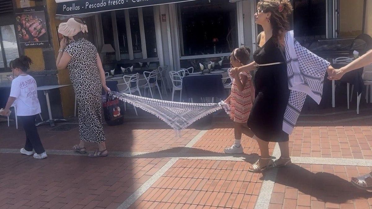 Una niña en la cadena en solidaridad con Palestina, unida a una mujer por una kufiya.