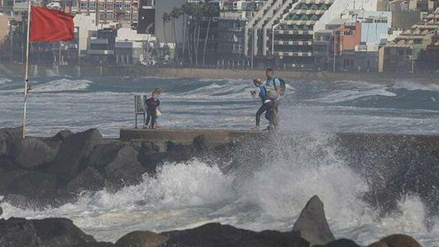 Varias personas se toman fotografías en el paseo de la playa de Las Canteras en Las Palmas de Gran Canaria con el oleaje de fondo