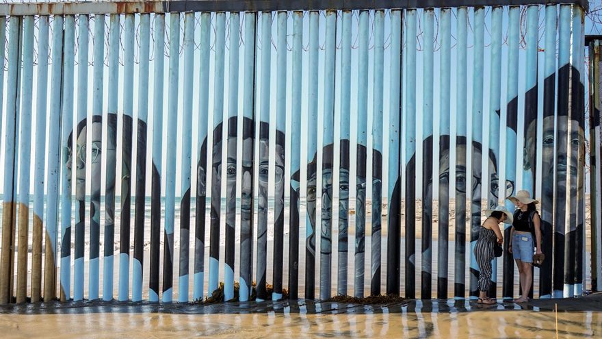 Personas caminan hoy junto a un mural con los rostros de personas deportadas pintado sobre la barrera metálica fronteriza en Tijuana, estado de Baja California (México). EFE/Joebeth Terriquez