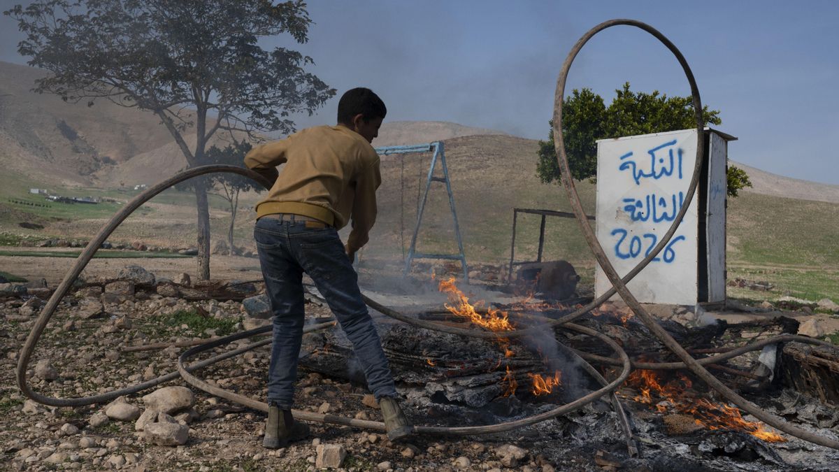 Un niño quema en una hoguera el 25 de enero una manguera de plástico que extrajo de la que era su vivienda junto a una pintada en la que se puede en árabe 'Nakba 2026'.