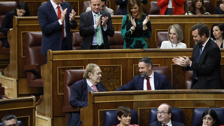 El profesor Ramón Tamames (i), acompañado por el líder de Vox, Santiago Abascal (c), mientras recibe los aplausos de los diputados de la formación política tras intervenir durante la segunda y última jornada del debate de la moción de censura que impulsa Vox.