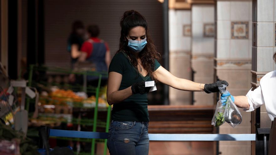 Una mujer atiende a una clienta en un puesto de frutas y verduras en un mercado.