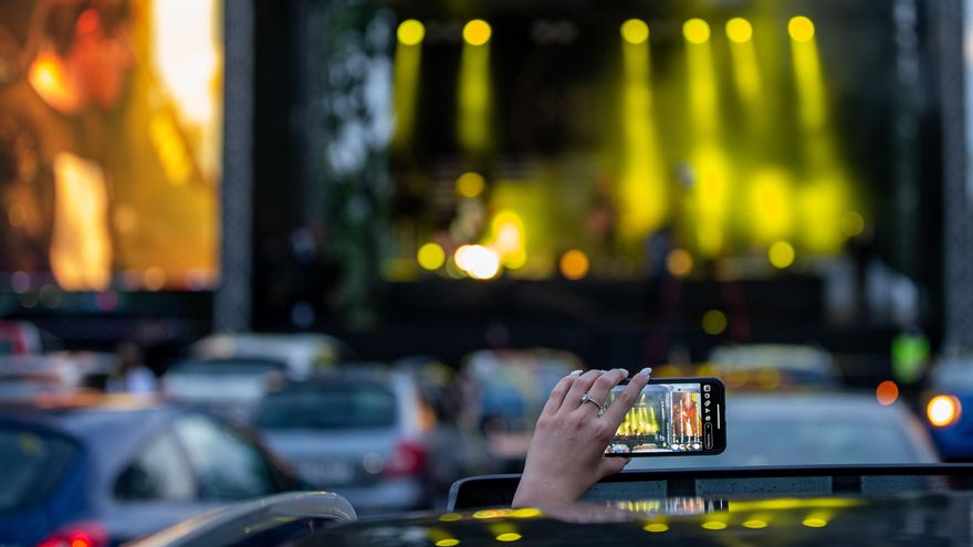 Una mujer sentada en su automóvil usa su teléfono móvil para grabar a una banda tocando en el escenario durante un concierto en un área abierta en Ostrava, República Checa.