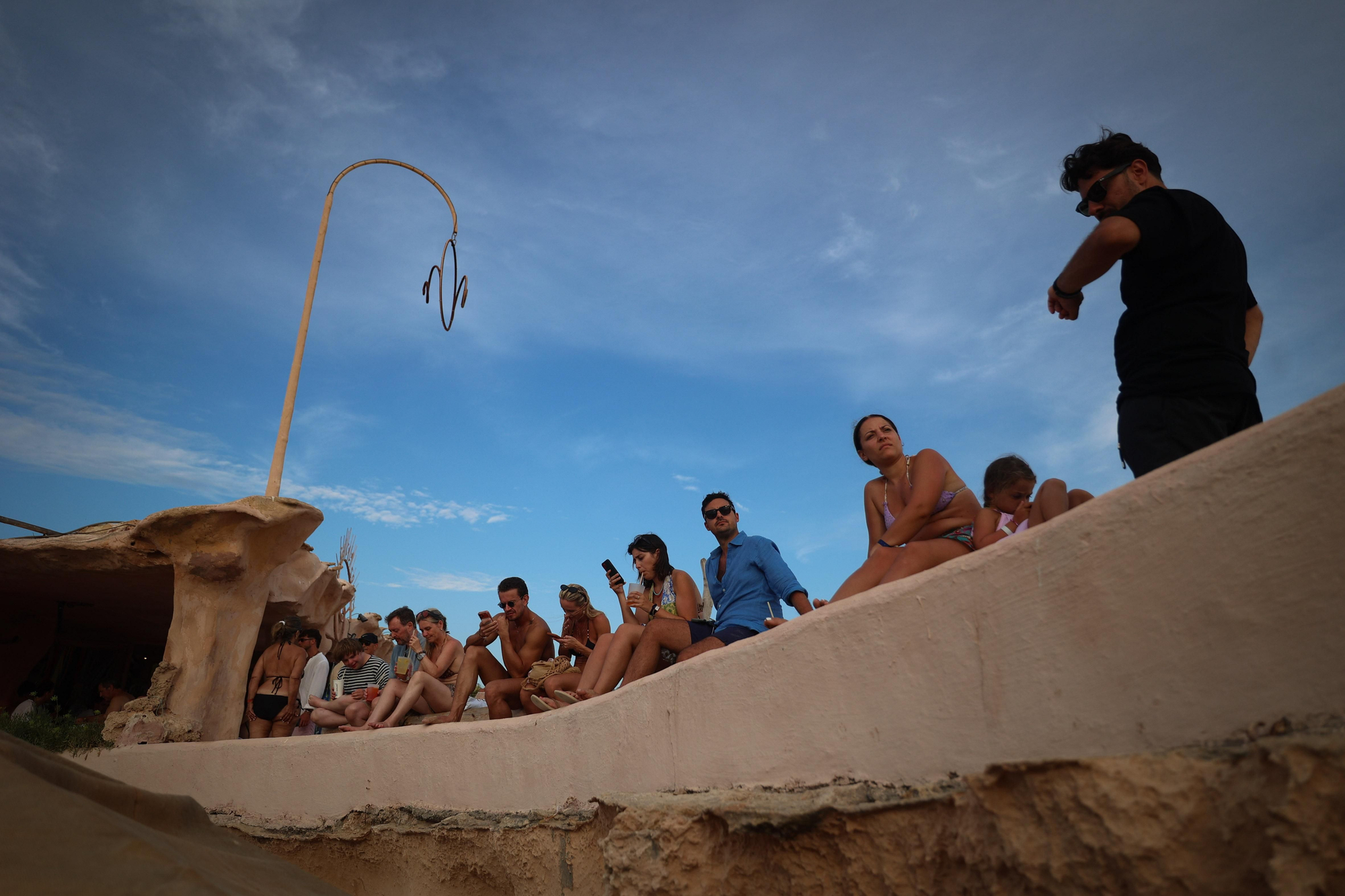 Un grupo de turistas escoge los acantilados que dividen las calas para ver la puesta de sol