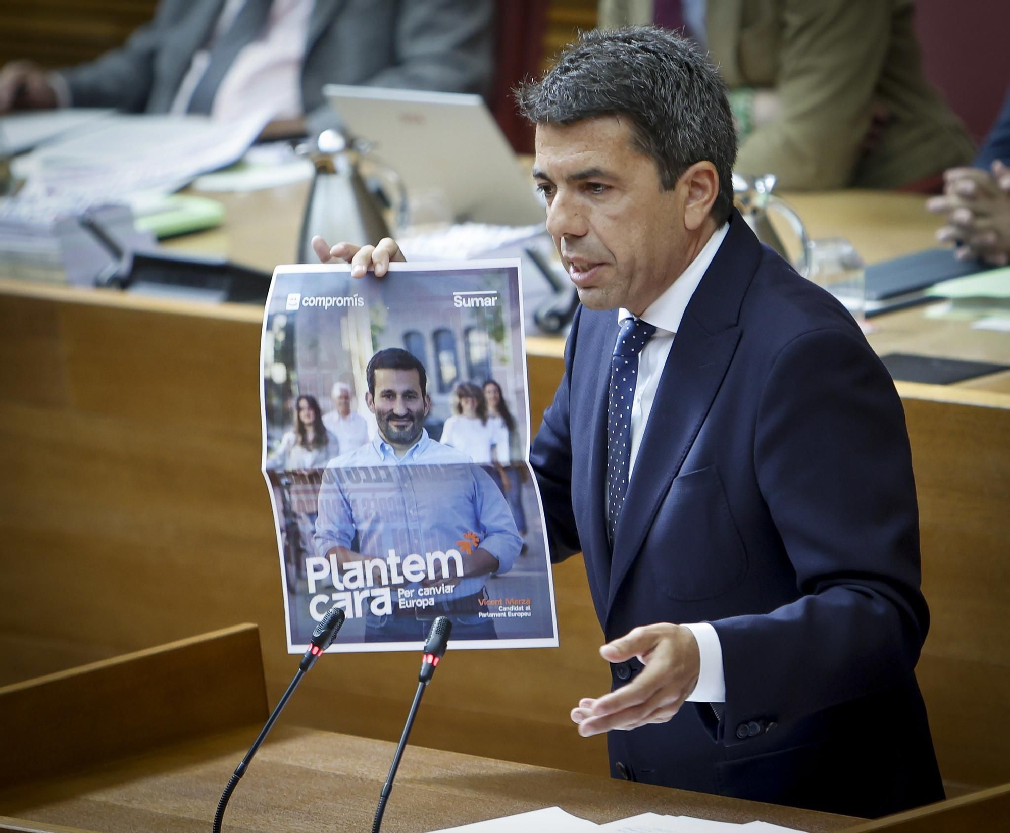 El presidente de la Generalitat Valenciana, Carlos Mazón, enseña el cartel electoral de Compromís-Sumar en las Corts Valencianes.
