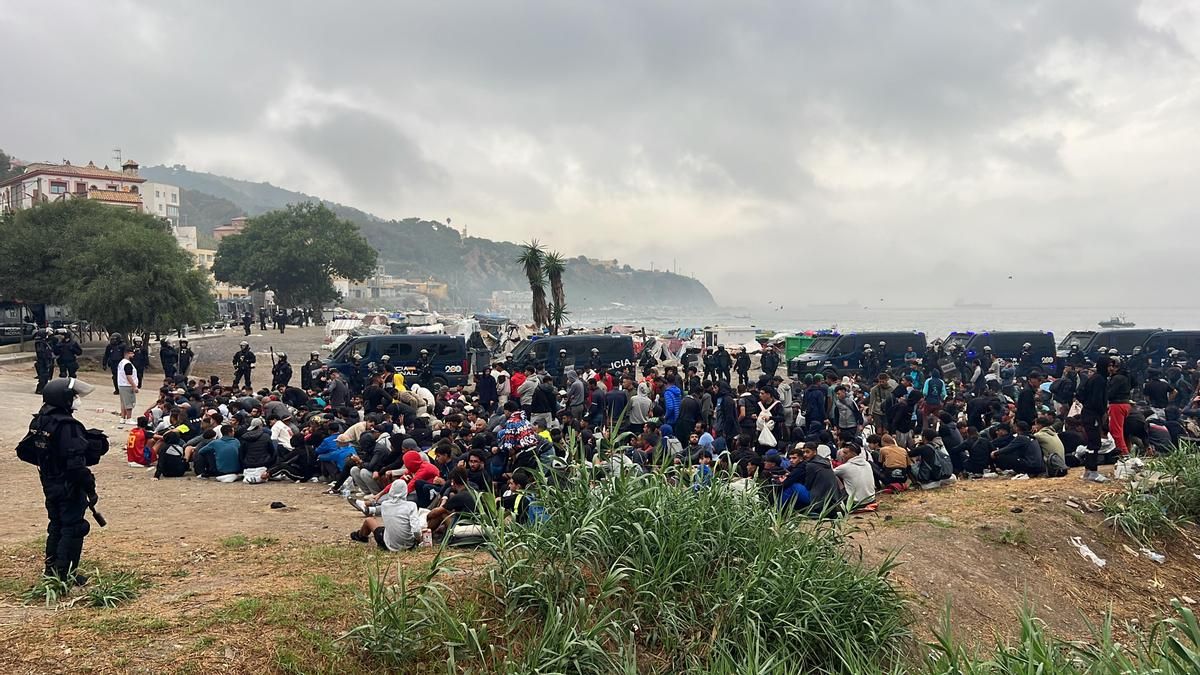 Decenas de personas migrantes aguardan el operativo policial desplegado en la Playa del Trampolín, en Ceuta. Soraya Aybar Laafou