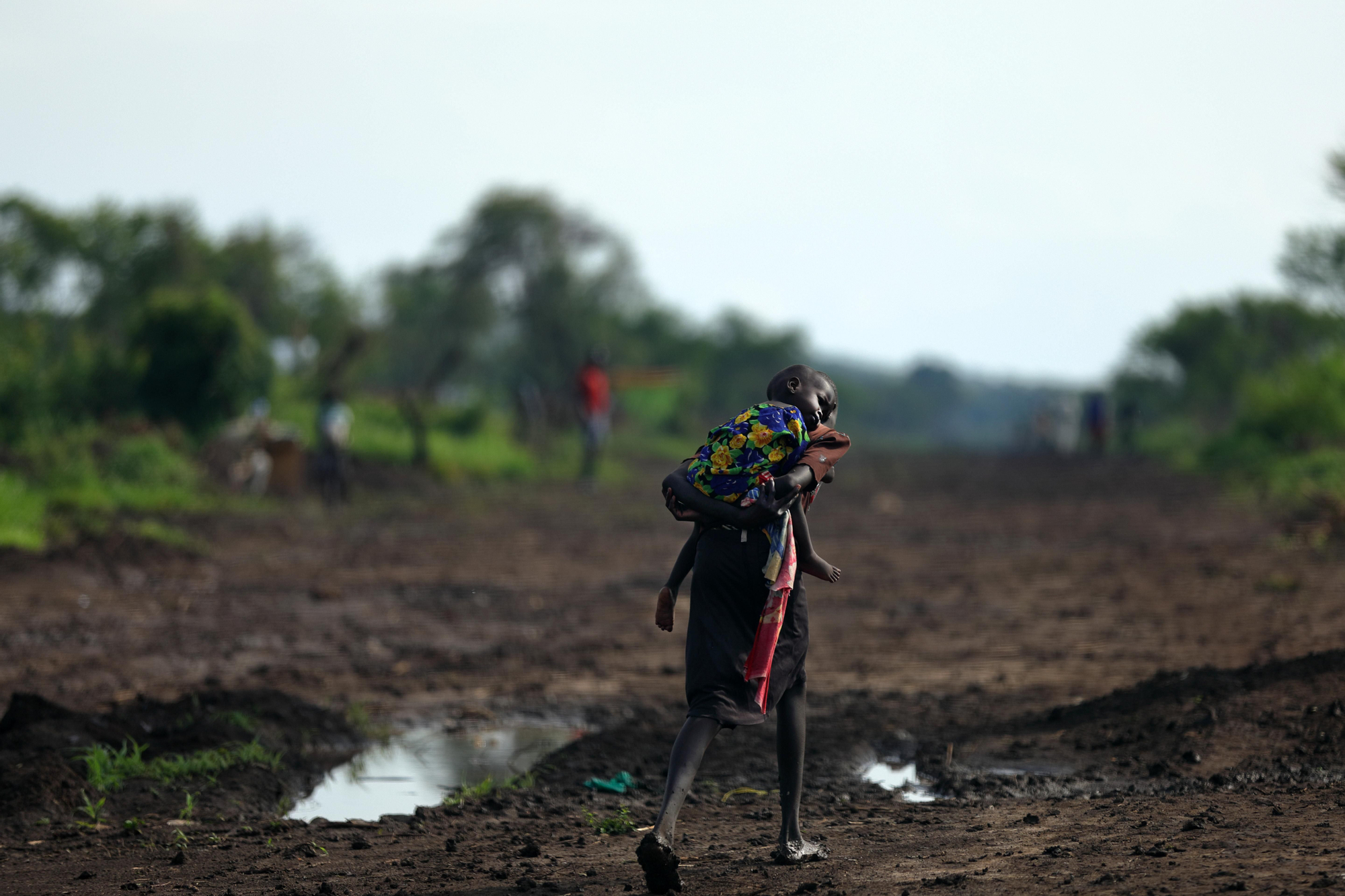 Una chica y su hermano, de Sudán del Sur, andan por un camino fangoso. Compartieron el alimento que recibieron. Fotografía: Atsushi Shibuya/MSF
