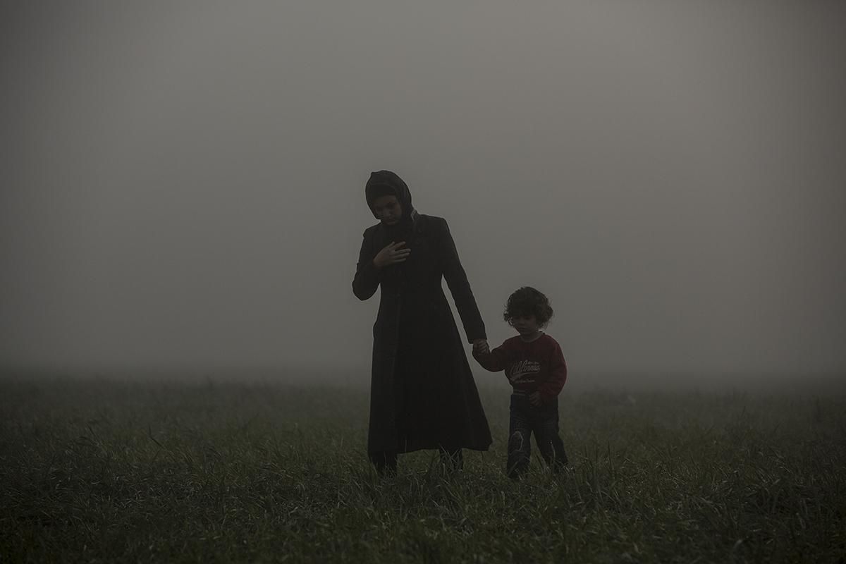 Una madre y su hijo caminando en los alrededores del campo improvisado de Idomeni durante una mañana con mucha niebla. Este campamento, al norte de Grecia junto a la frontera de Macedonia, llegó al albergar a unas 14.000 personas. Idomeni, 08/03/2016. | OLMO CALVO