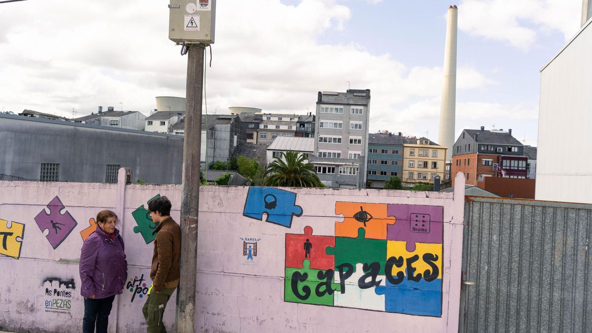 Dos personas hablan ante un mural en el centro urbano de As pontes