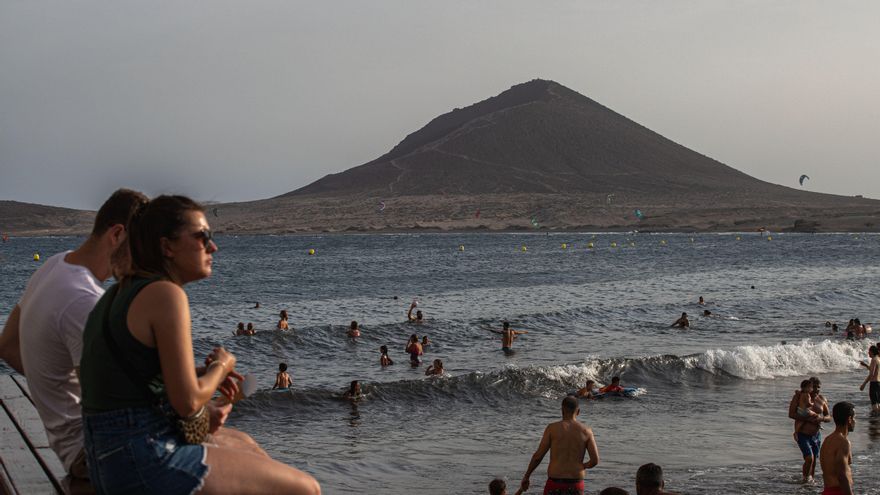 Varias personas disfrutan del baño en El Médano mientras de fondo se practican deportes acuáticos
