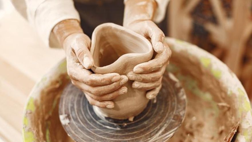 Manos de alfarero o alfarera trabajando arcilla en el torno