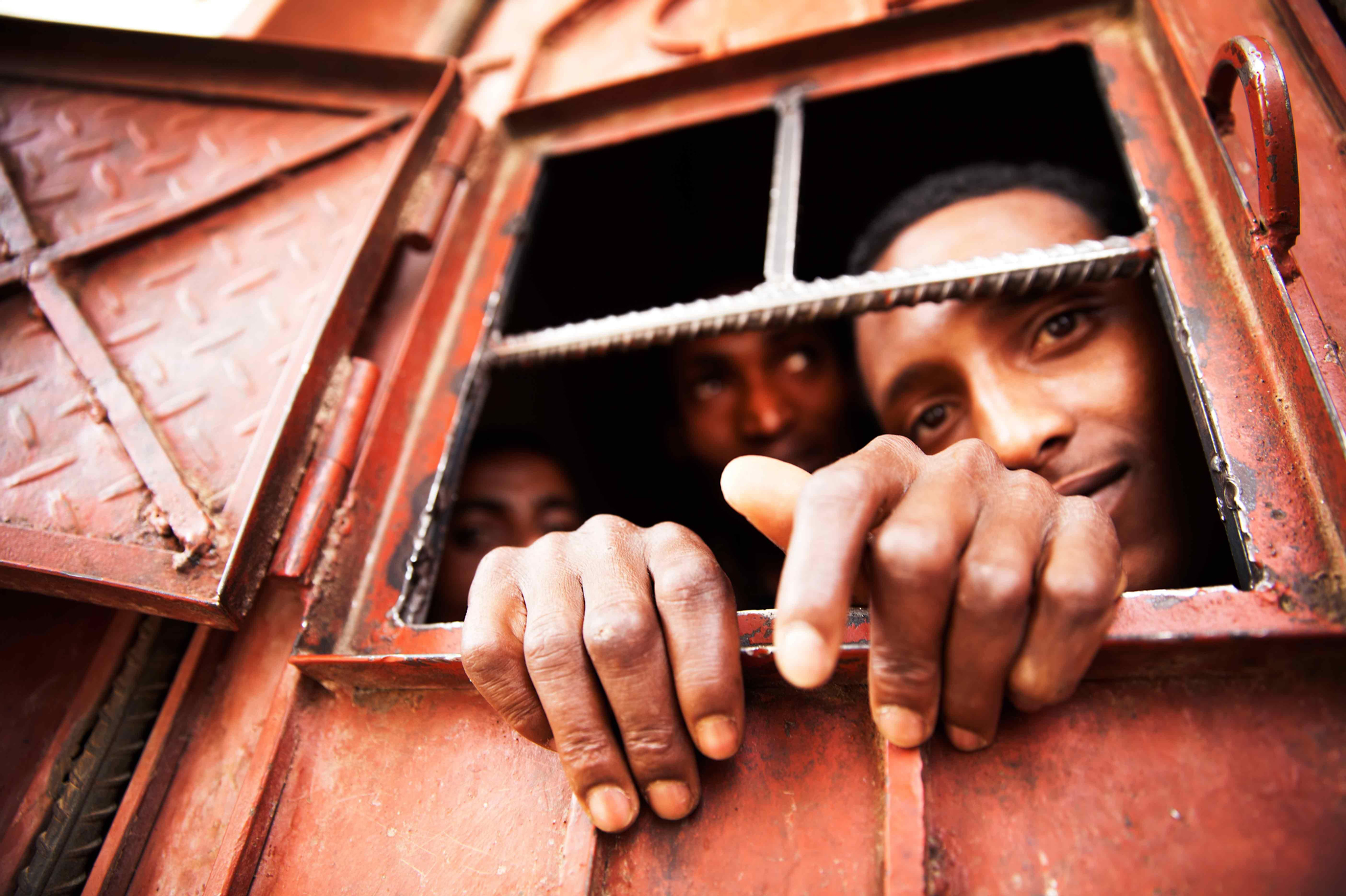 Varios inmigrantes se asoman por la pequeña ventana de una de las celdas del centro de detención de Saná. / Copyright: Anna Surinyach/MSF