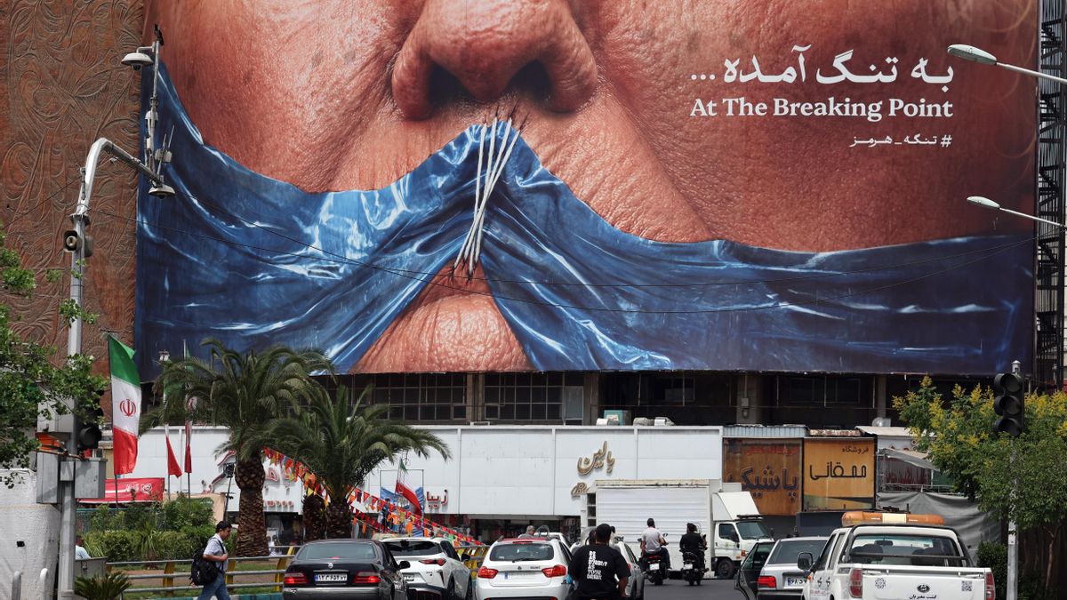 Iraníes conducen frente a un gran cartel antiestadounidense que muestra a Donald Trump y el estrecho de Ormuz en la plaza Valiasr en Teherán