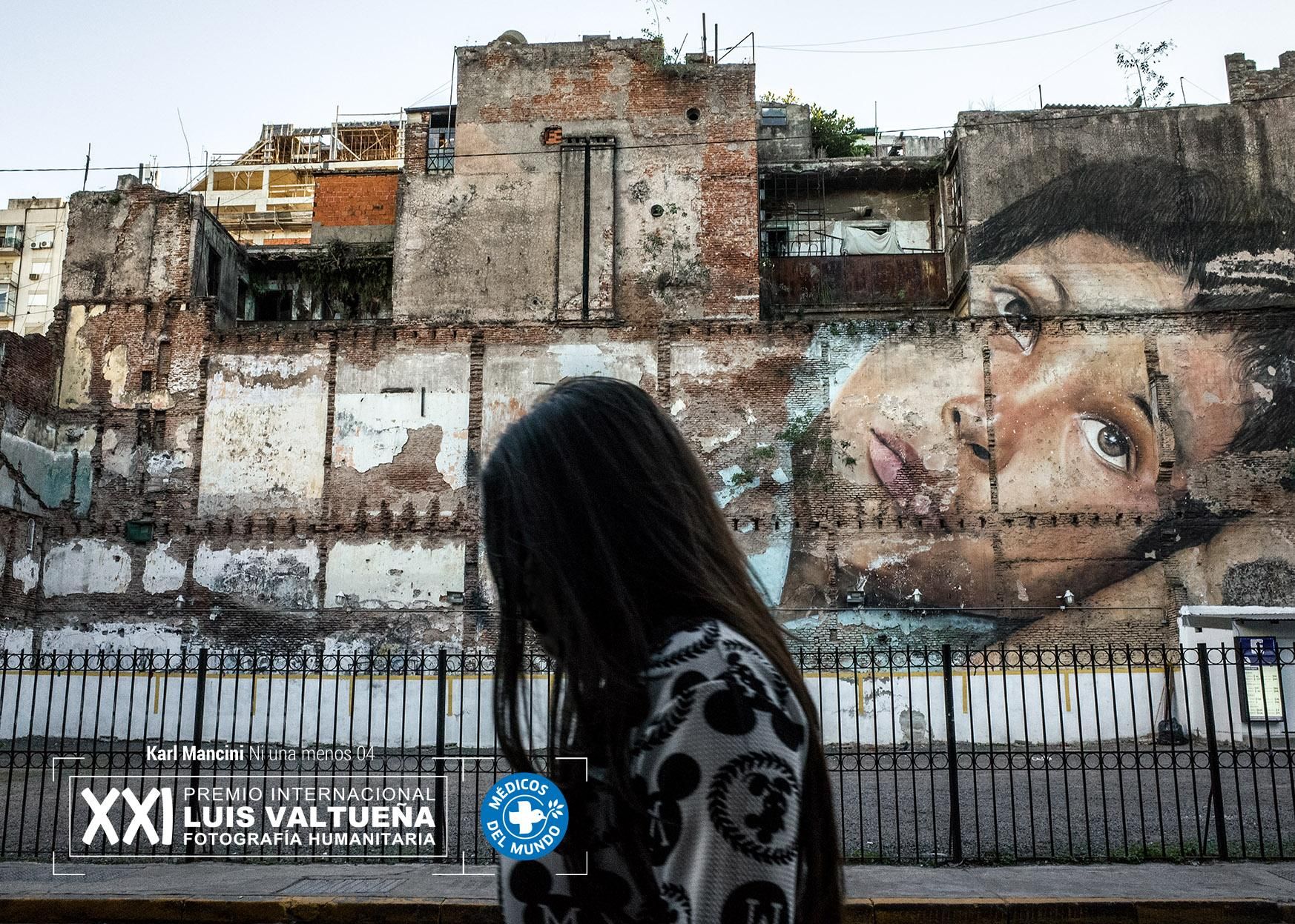 Buenos Aires. Una mujer camina en una calle del centro con un gran mural al fondo. Toda la ciudad está llena de paredes pintadas, a veces edificios enteros o calles. A menudo estas pinturas son políticas, muchas están en contra de la violencia de género, la injusticia y las personas desaparecidas. Foto: Karl Mancini. NI UNA MENOS. Segundo finalista.