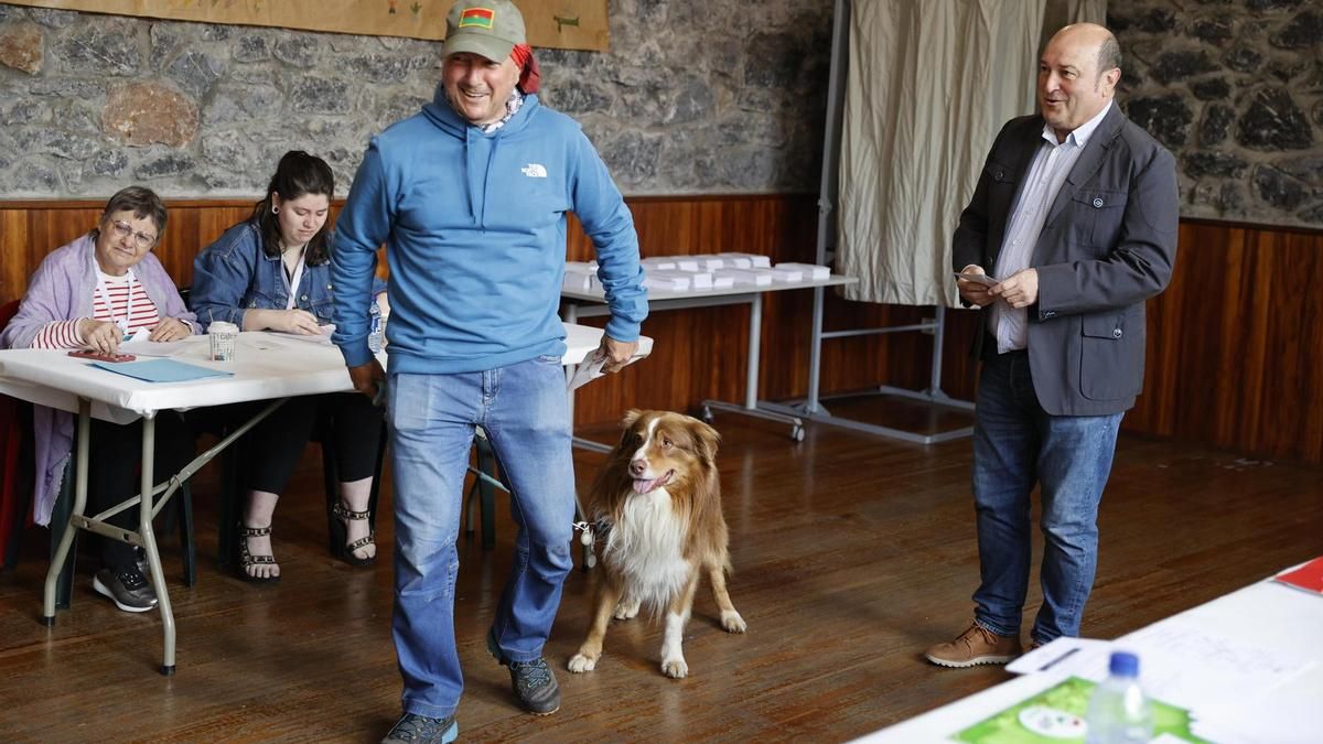 Un hombre vota con su perro junto a Andoni Ortuzar en un colegio electoral de Sanfuentes (Bizkaia)