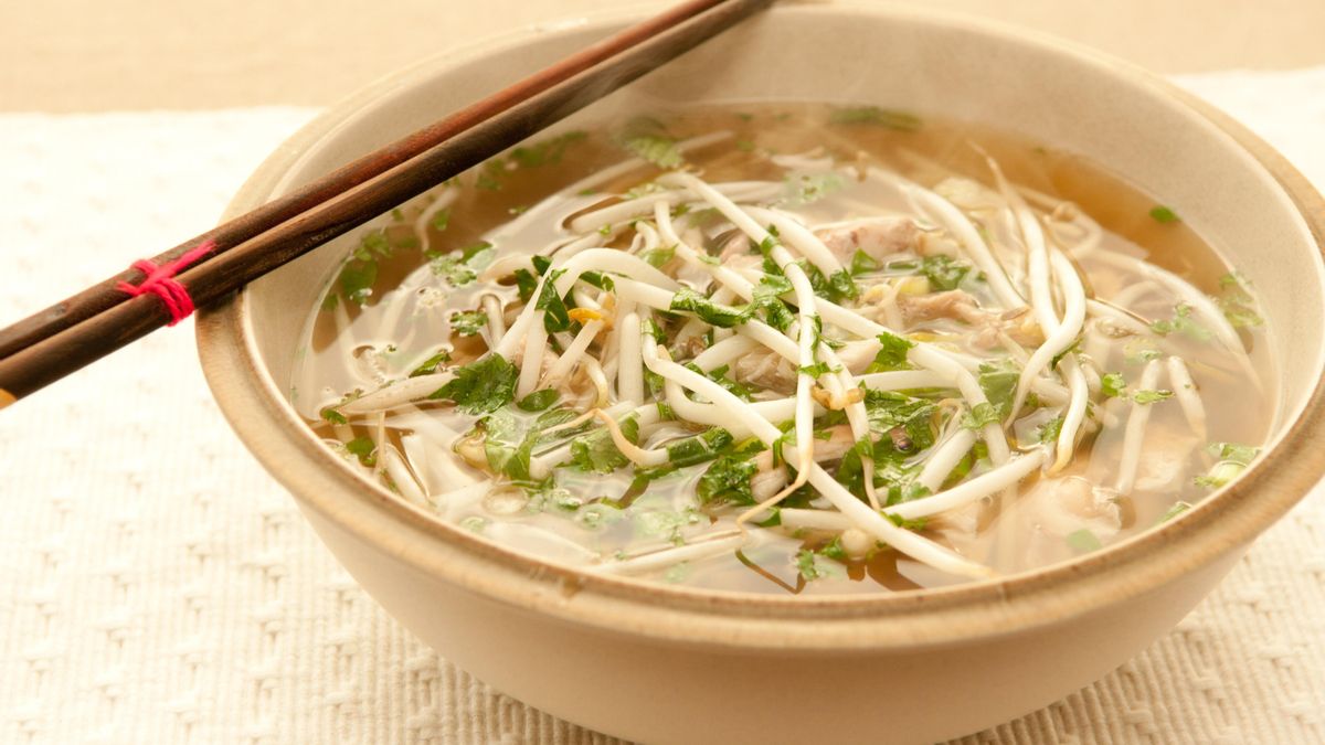 Tazón de sopa con caldo fideos de arroz y carne.