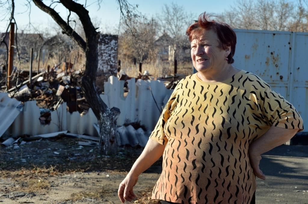 Galina, de 64 años, se encuentra delante de la casa destruida de su vecino en Debaltsevo, una localidad de Donetsk golpeada duramente por el conflicto. Mientras las personas con recursos se han marchado a Rusia o a otras zonas de Ucrania, muchos como Galina siguen viviendo con el constante temor de ser bombardeados.   “Nos escondimos en el sótano desde donde oíamos las explosiones muy cerca. Las bombas cayeron en nuestra calle e incendiaron la casa que se encuentra frente a la mía. Los bomberos no pudieron llegar porque el bombardeo causó  muchos otros incendios". Fotografía: Julie Rémy / MSF