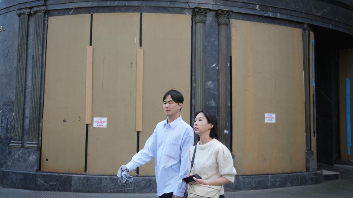 Dos turistas pasean junto a una tienda con los escaparates tapados en Barcelona.