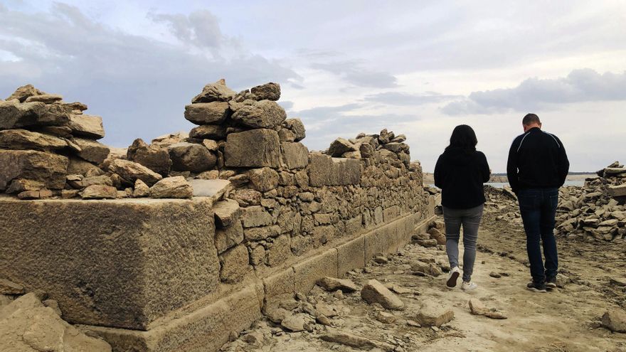 Dos visitantes recorren los restos de la localidad desaparecida, junto al muro de una antigua casa.