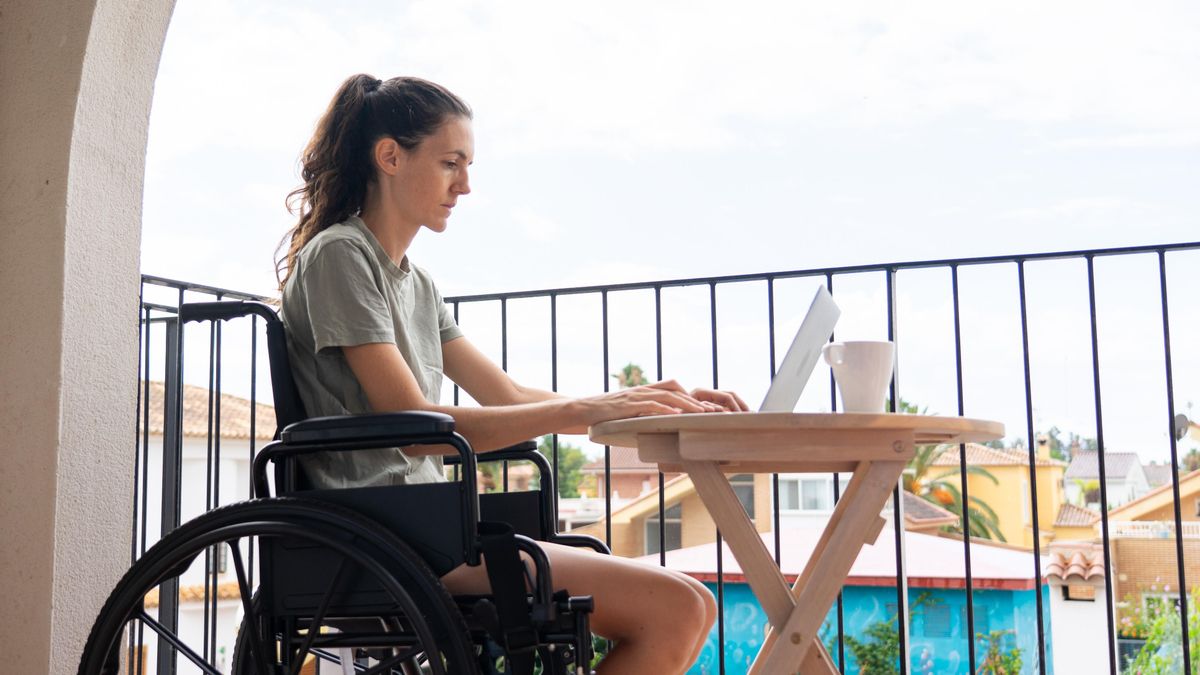 Una mujer en silla de ruedas trabaja desde la terraza de su habitación de hotel.