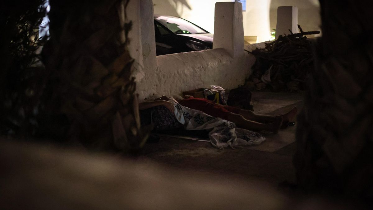 Dos ciudadanos se acomodan en el suelo, en las inmediaciones de la Iglesia de la localidad.