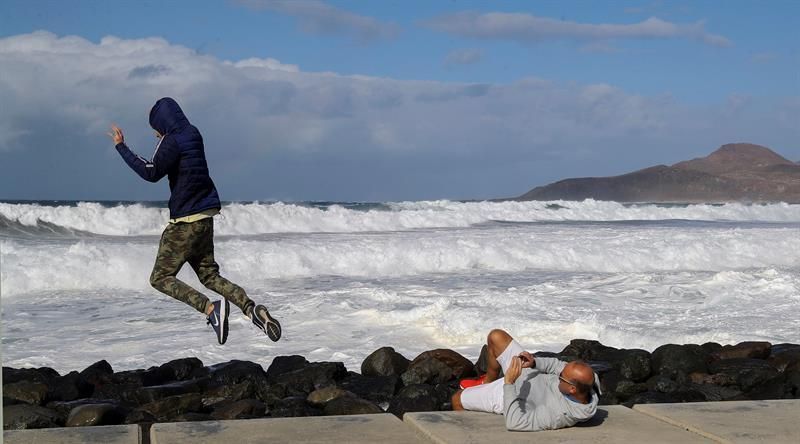 Dos personas se toman fotografías con el oleaje de fondo en el paseo de la playa de Las Canteras en Las Palmas de Gran Canaria. EFE/Elvira Urquijo A.