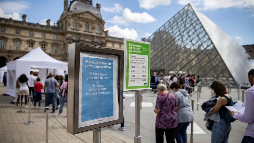 Turistas con mascarillas hacen cola en la entrada del museo 'Louvre', al lado de una señal que indica la necesidad del pasaporte sanitario para ingresar al complejo.