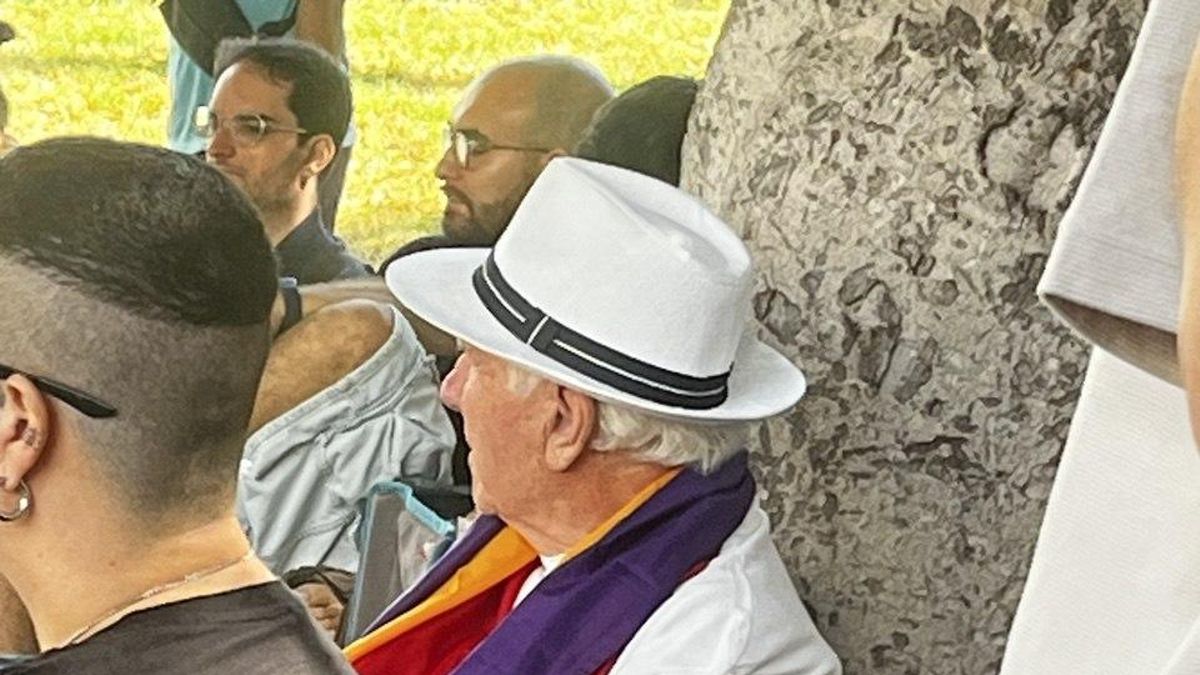 Un hombre atiende a lo que se dice en la asamblea sentado a la sombra de un árbol.