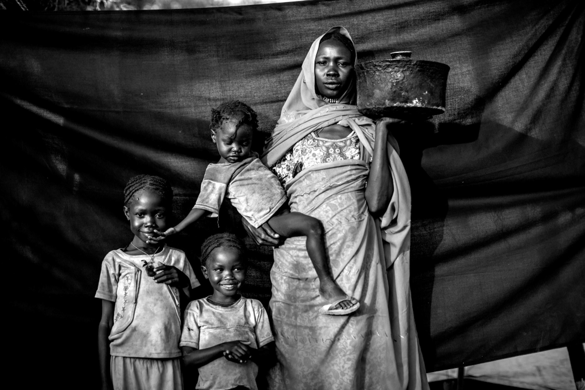 Magboola, 20 años, en el campamento de refugiados de Jamam, Maban, Sudán del Sur. Ella y su familia resistieron varios ataques aéreos durante meses, pero decidieron huir de su pueblo, Bofe, la noche en que los soldados se presentaron en él abriendo fuego. Lo más importante que se llevó consigo es la olla que sostiene en esta fotografía, para cocinar el sorgo para ella y sus tres hijas durante el viaje. / Brian Sokol.