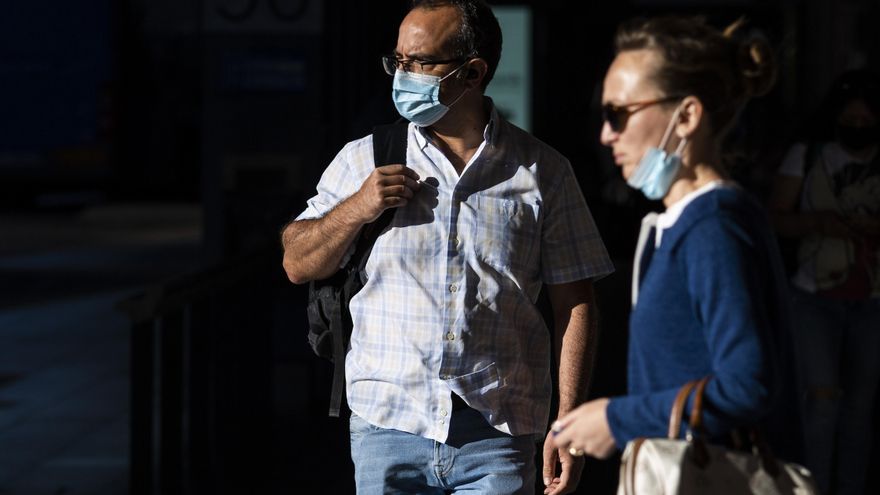 Un hombre y una mujer, con y sin mascarilla en una calle.
