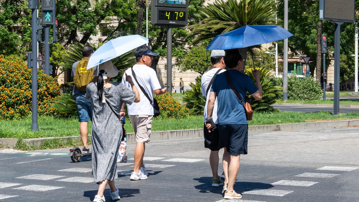 Turistas pasando junto a un termómetro en las calles de Sevilla en plena ola de calor