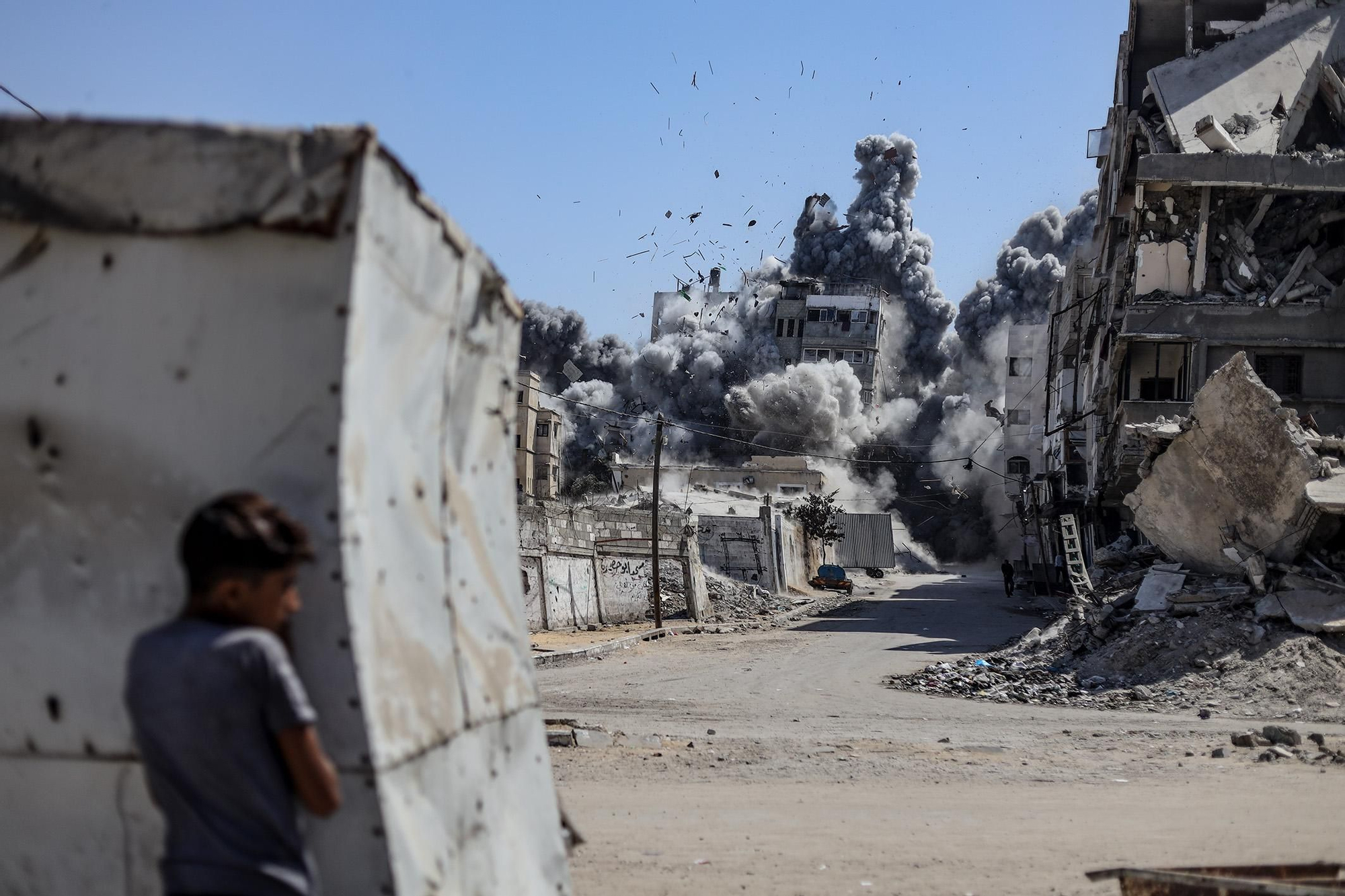 En la ciudad de Gaza, un niño observa a distancia cómo una densa columna de humo se eleva desde un edificio alcanzado por un misil. 27 de septiembre de 2025. © Khames Alrefi. Ganador del Premio Visa d’Or Humanitario 2026 del Comité Internacional de la Cruz Roja (CICR).