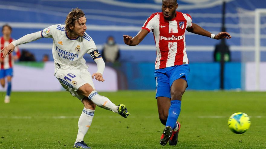 MADRID, 12/12/2021. El centrocampista croata del Real Madrid, Luka Modric (i), golpea el balón ante el centrocampista francés del Atlético de Madrid, Geoffrey Kondogbia, durante el encuentro correspondiente a la decimosexta jornada de primera división que disputan hoy domingo en el estadio Santiago Bernabéu, en Madrid.