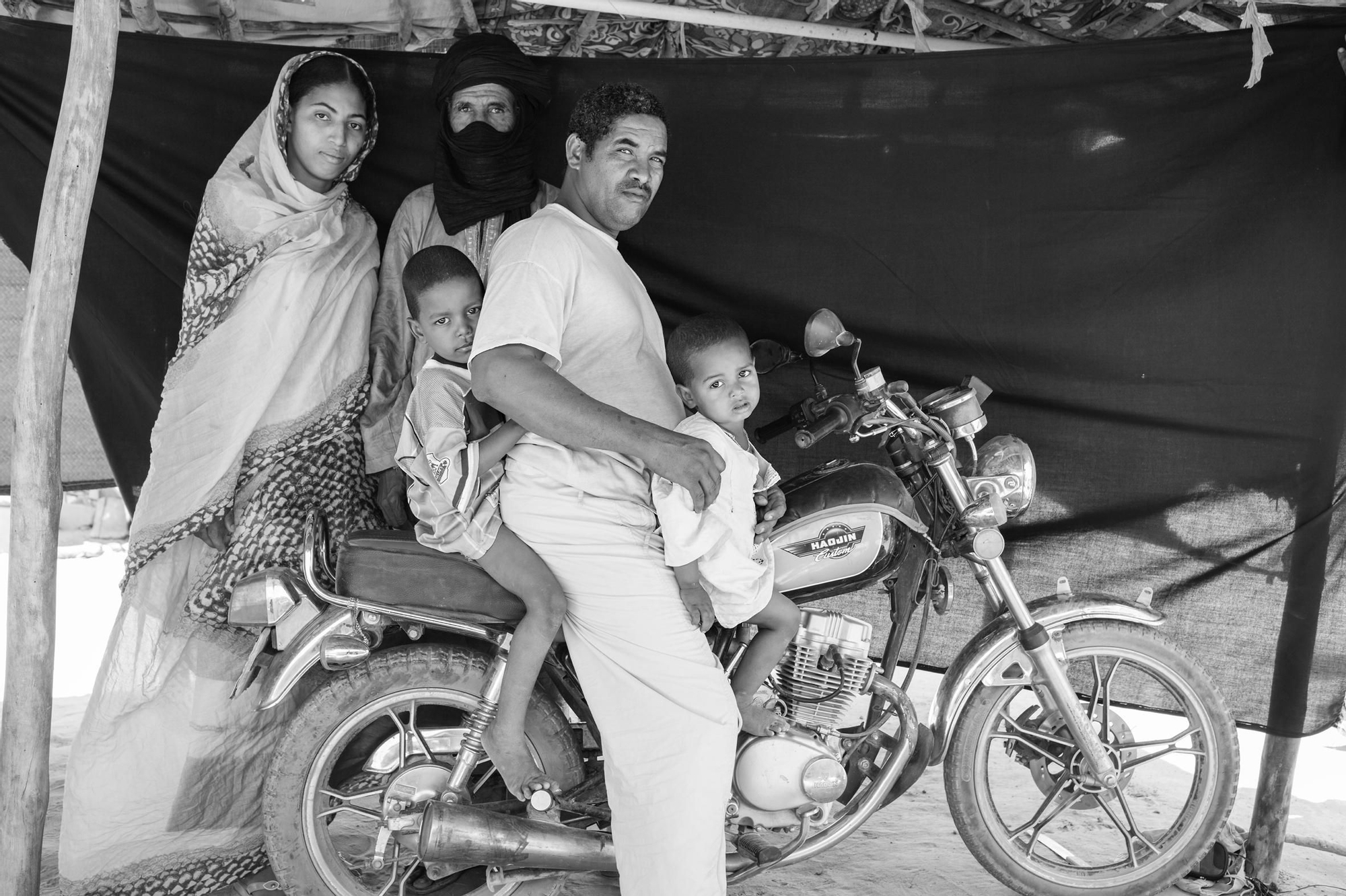 Abdou Ag Moussa, 34 años, en el campo de refugiados de Mentao, Burkina Faso. Abdou está sentado junto a su familia sobre la moto que asegura que le salvó la vida. La familia de Abdou huyó de su casa en Malí después de que su madre y otras cuatro mujeres fueran secuestradas, llevadas al desierto y asesinadas. / Brian Sokol.